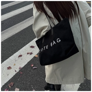 Street style shot of a black canvas tote bag with bold white text worn on the shoulder