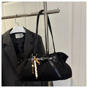 Detail of black suede tote bag with pleated design and decorative wooden bead pendant