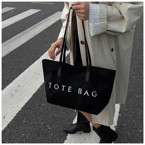 Detail der schwarzen Canvas-Tragetasche mit weißem TOTE BAG Aufdruck und Ledergriff