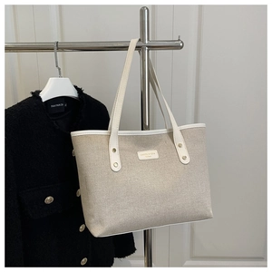 Detail of beige canvas tote bag with white leather trim and brand metal plate