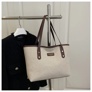 Detail of canvas tote bag with brown leather handles and brand logo plate
