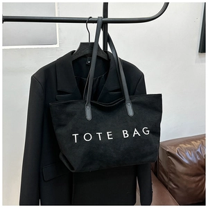 Close-up of black suede tote bag with white TOTE BAG text and leather shoulder strap