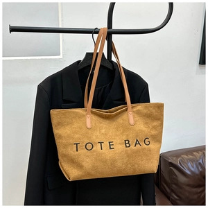 Close-up of camel suede tote bag with black TOTE BAG embroidery and slim leather handles