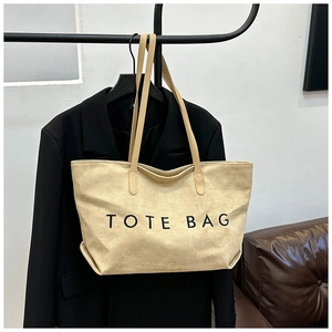 Detail of beige canvas tote bag with black TOTE BAG print and leather handles