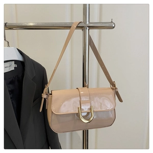 Detail van beige laks leren handtas met een opvallende gouden hoefijzer sluiting