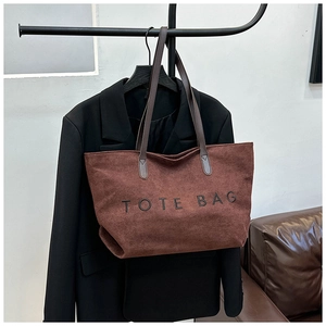 Detailed close-up of a brown suede tote bag with black embroidery on a hanger