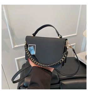 Close-up of black square bag with golden chain and blue textured metallic buckle detail