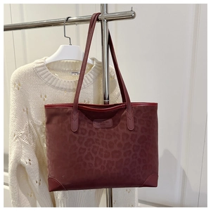 Detail of burgundy leopard embossed tote bag with metal brand tag and reinforced corners