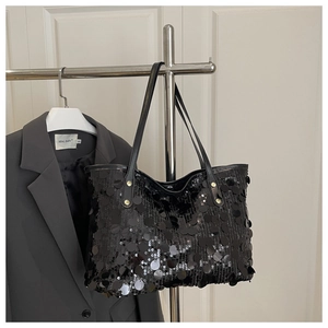 Detail of black sequined tote bag featuring leather handles and golden rivets