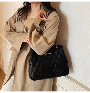 Détail du sac cabas matelassé noir avec chaîne dorée et logo sur un trench-coat beige