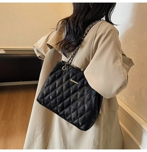 Vue détaillée d'un sac bandoulière matelassé noir avec chaîne dorée sur un trench beige