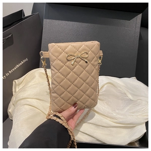 Détail d'un mini sac à bandoulière matelassé beige avec nœud doré et bandoulière chaîne