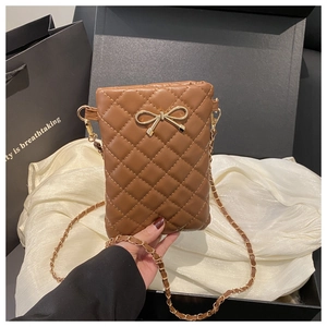 Détail du sac bandoulière matelassé marron avec nœud doré sur fond de soie