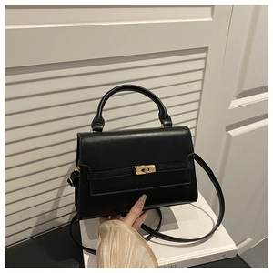 Detail of structured black handbag with gold twist lock and adjustable shoulder strap