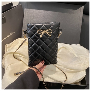 Détail d'un mini sac matelassé noir avec fermoir noeud doré sur tissu de soie blanc