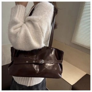 Détail d'un sac à épaule marron foncé brillant avec boucle argentée et ceinture