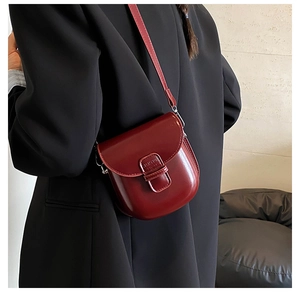 Close-up of a vintage red leather saddle bag with adjustable strap worn by a model
