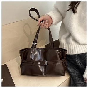 Detail of vintage brown glossy tote bag with decorative buckle straps and adjustable handles