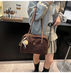 Detail of dark brown suede shoulder bag with leather straps and decorative fur ball charm
