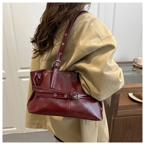 Detail view of burgundy glossy leather shoulder bag with metallic eyelet strap and buckle