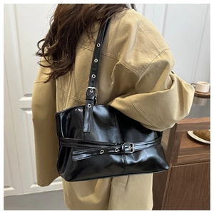 Detail of glossy black leather underarm bag with silver buckles and moto-style studs