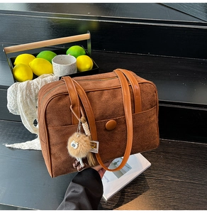 Detail of dark brown suede handbag with plush owl pendant and leather straps on wood steps