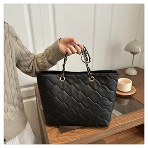 Detailansicht einer schwarzen Stepptasche mit goldener Kette auf einem Vintage-Tisch