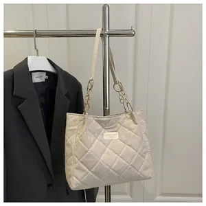 Detail of beige quilted tote bag featuring chain strap and leather brand name tag