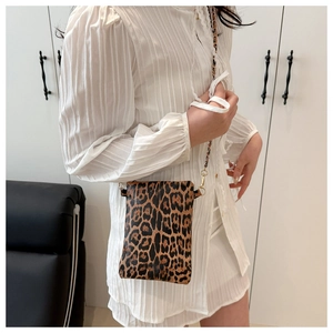 Detail of leopard print crossbody bag with gold chain strap worn by a model in white dress