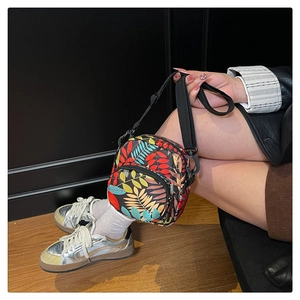 Model view of a compact crossbody bag featuring colorful tropical leaf patterns and zipper