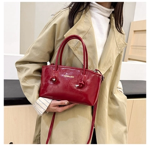 Detail of red patent leather tote bag featuring knot handle design and gold lettering