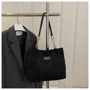 Detail of black quilted tote bag with golden logo plaque and metal chain strap