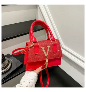 Detail of red leather bag featuring a gold V-logo, metallic tassel and glitter texture