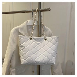 Detailed view of quilted white tote bag with gold chain strap on a clothing rack