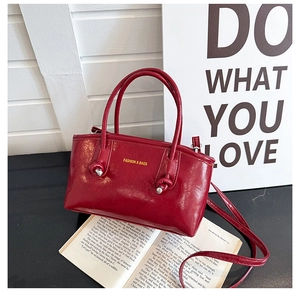 Detail of red glossy tote bag with decorative knot and long shoulder strap on a black table