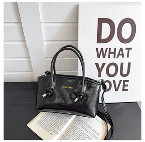 Detail of glossy black tote bag with gold lettering and silver metal handle accents