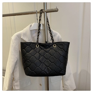 Close-up of black quilted tote bag with golden metal chain and diamond stitching detail