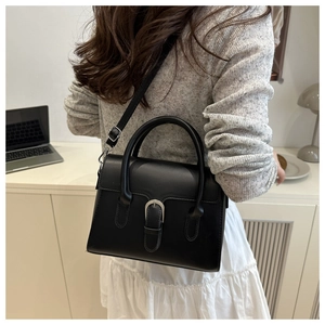 Detail of black textured leather bag with silver buckle worn as a crossbody accessory