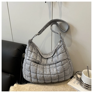 Detail of grey quilted puffy hobo bag with adjustable strap on a soft knit blanket