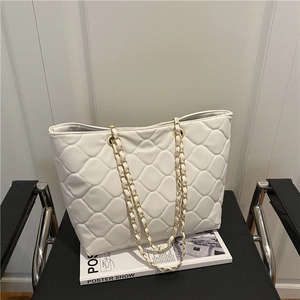 Chic white quilted tote bag with diamond pattern and metal chain strap on a black chair