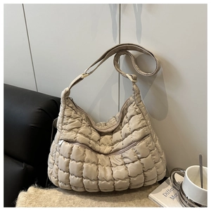 Macro view of quilted beige puffer shoulder bag with square padding and zipper detail