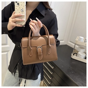 Detail of a brown leather handbag featuring a silver buckle and dual carry handles