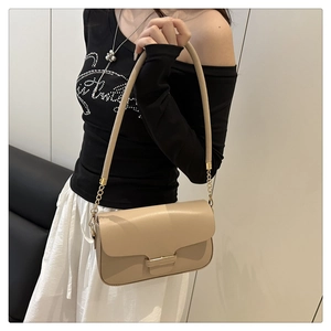 Detail view of beige leather shoulder bag with golden chain strap on a stylish model