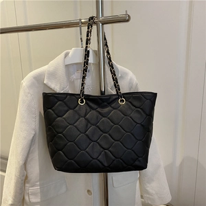 Quilted black tote bag with gold chain strap shown hanging in a stylish lifestyle setting