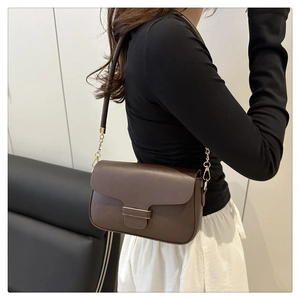 Détail d'un sac bandoulière en cuir marron foncé avec boucle dorée porté par un modèle
