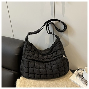 Detail of black quilted puffer bag with zipper pocket and adjustable strap on beige rug