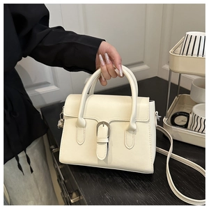 Detail of cream leather handbag showing top handle and silver buckle on a table