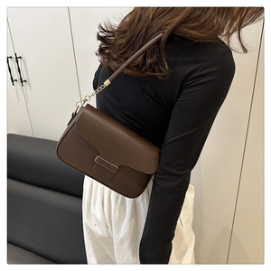 Détail du sac à bandoulière en cuir marron foncé avec chaîne dorée porté par un mannequin
