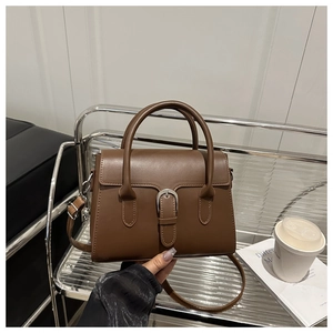 Detailed close-up of brown leather bag with silver metal buckle on a designer shelf