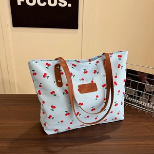 Sac fourre-tout bleu clair à imprimé cerise avec poignées en cuir sur table en bois
